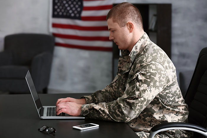 Man in military uniform working on a laptop to find a job in insurance. He seems impressed with TDI’s website.