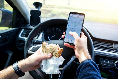 Distracted driving, holding a phone and a sandwich.