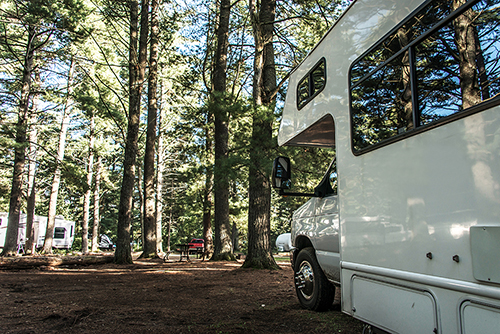 RV parked at a campground with fire pit in view. Unseen driver inside probably reading about RV fire safety tips.
