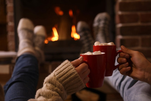 A couple sipping hot chocolate by the fireplace.